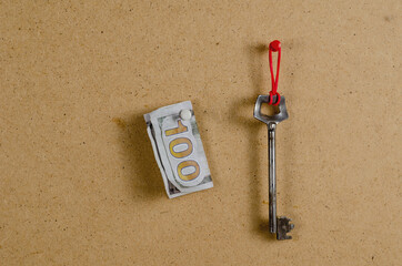 A large metal door key and money against a brown background. The