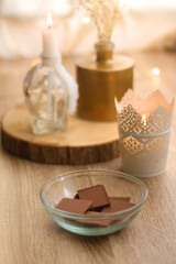 Bowl of chocolate, book, reading glasses, candles and vase with flowers on the table. Selective focus.