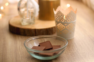 Bowl of chocolate, book, reading glasses, candles and vase with flowers on the table. Selective focus.