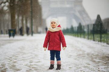Adorable toddler girl near the Eiffel tower on a day with heavy snowfall in Paris, France