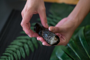 Fototapeta premium The process of making and decorating tuna Temaki Hand Roll. Hand Cooking Temaki Tuna Sushi in Japanese restaurant. Black background with green plants 