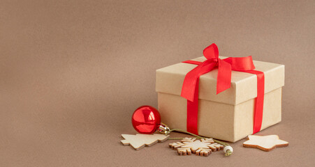 Gift box with red ribbon and Christmas ornaments on brown background