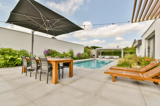 Sunbeds and dining zone near pool in backyard of modern house