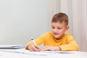 Naklejka premium schoolboy do lessons and writes tasks to notebooks at home. homeschooling, distant learning 