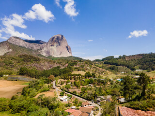 Visão aérea da Pedra Azul, com vegetação, casas, vilarejo e igreja. Na região de montanhas em...