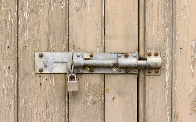 Close up of an old weathered wooden door with flaking paint with bolt and locked padlock. UK