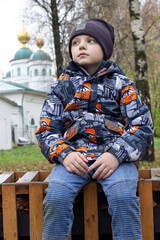 a boy sits on a bench in an autumn park against the background of a church