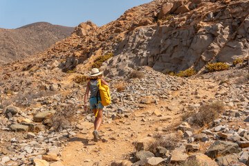 A young woman walking along the canyon path towards the Mirador de la Peñitas, west coast of the island of Fuerteventura, Canary Islands. Spain
