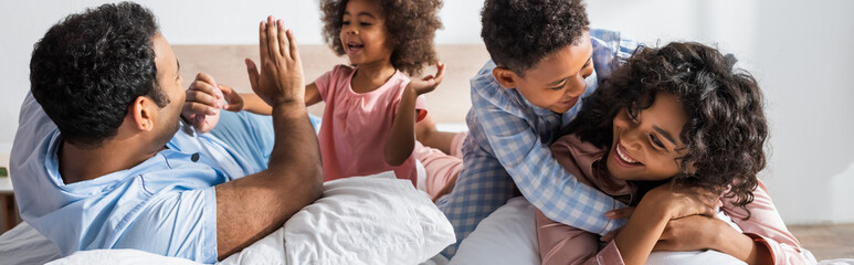 african american boy embracing mother near dad and sister playing patty cake game in bedroom, banner