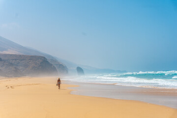 Fototapeta na wymiar Tourist girl with a hat walking alone on the Cofete beach of the natural park of Jandia, Barlovento, south of Fuerteventura, Canary Islands. Spain