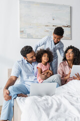 african american couple using laptop and digital tablet neat happy kids in bedroom