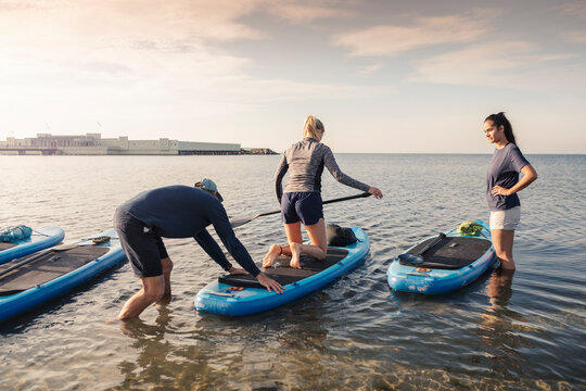 Male instructor teaching paddleboarding to women in sea