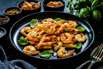 Penne with fried prawns in on black wooden background
