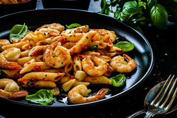 Penne with fried prawns in on black wooden background
