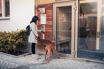 Woman entering password to open door while standing with dog at entrance of apartment