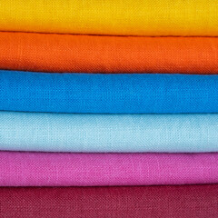 A stack of multi-colored bright linen fabric, close-up. Linen background. Fabric stripes