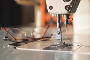 Industrial sewing machine needle steel presser foot with white thread for sew cloth with glasses vintage tone close-up.