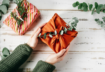 Furoshiki tissue wrapping of presents. Female hand holding a gift in eco friendly reusable fabric...