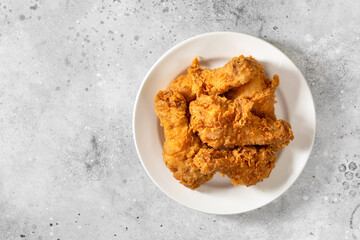 Fried crispy chicken legs in breadcrumbs in a white plate on a light culinary background. Fast food from the drumstick top view	