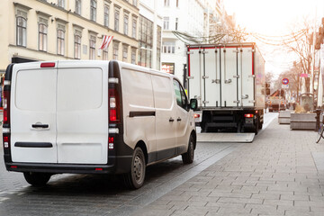 Small white van and mid size cargo truck parked for unloading at european old city street road....