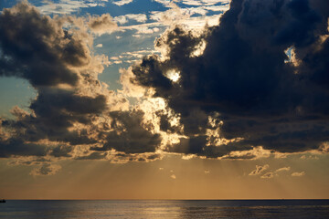 Sunset sky with dark clouds and sunbeams over the ocean.