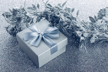 Small gift box with satin bow and artificial silver flowers decoration on silver glitter background