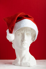 Gypsum copy of the sculpture David Michelangelo wearing a red christmas Santa Claus hat on red...