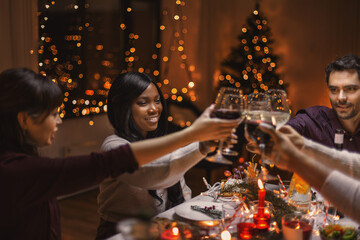 holidays, party and celebration concept - multiethnic group of happy friends having christmas dinner at home and drinking wine