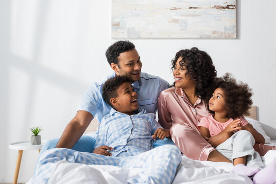 happy african american couple talking in bed near cheerful kids