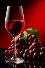 A glass of red wine and grapes on a glossy table.