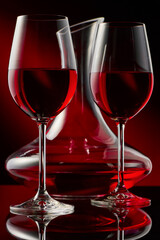 Still life with a decanter and two glasses of red wine on a glossy table.