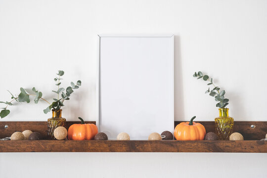 White mock up picture frame on brown shelf with decorative pumpkins and lights. Copy space