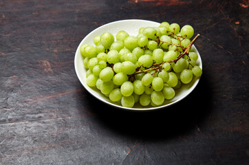 Branch of ripe green grape on plate with water drops. Juicy grapes on wooden background, closeup. Grapes on dark kitchen table with copy space