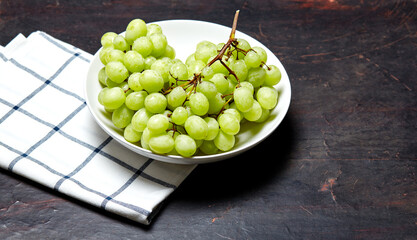 Branch of ripe green grape on plate with water drops. Juicy grapes on wooden background, closeup. Grapes on dark kitchen table with copy space