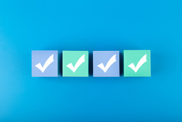 Four white checkmarks on multicolored cubes in a row against blue background 