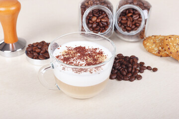 Cup of cappuccino, cookies, coffee beans and tamper on table.