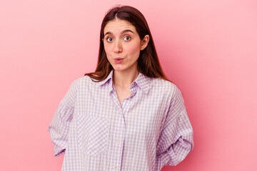 Young caucasian woman isolated on pink background shrugs shoulders and open eyes confused.