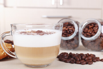 Cup of cappuccino with chocolate crumbs, cookies, and coffee beans on table.