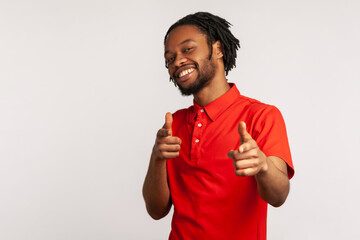 Portrait of man with dreadlocks wearing red casual style T-shirt, pointing finger pistols to camera...