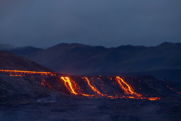 Hot landscape of an erupting volcano with fresh lava coming ot from the crater.