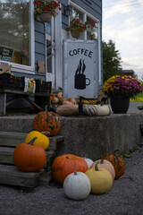 Sign coffee at the small village store with a few different large colorful pumpkins scattered at the porch. Selective focus.