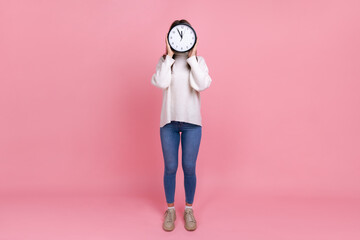 Full length portrait of unknown woman hiding her face behind big wall clock, showing time to go,...