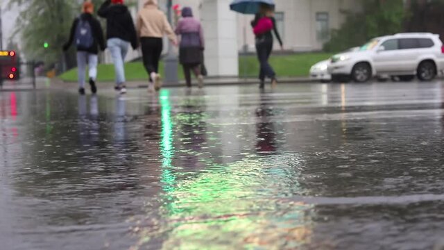 People are running along a pedestrian crossing in the rain. Rain. Close-up of raindrops falling on a pedestrian crossing. Pedestrian crossing in a big city. Rainy day. The asphalt is wet from the rain