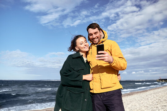 technology, relationships and people concept - happy couple with smartphone on autumn beach