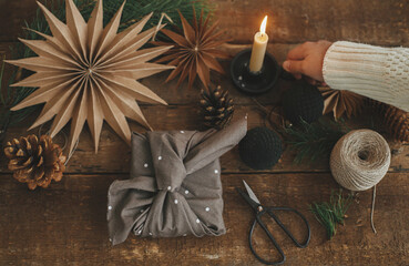 Christmas advent. Hand holding candle and stylish christmas gift wrapped in fabric, scissors, paper...