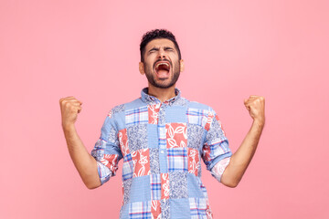 Portrait of overjoyed handsome man with beard in casual shirt expressing winning gesture with...