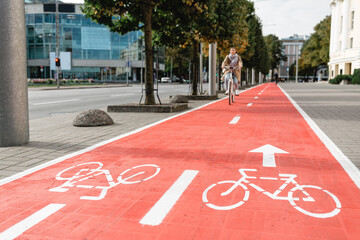 traffic, city transport and people concept - woman cycling along red bike lane with signs of bicycles and two way arrows on street - obrazy, fototapety, plakaty