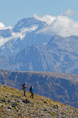 Fototapeta premium CHAMROUSSE, FRANCE, September 23, 2021 : Couple of hikers on the slopes, with high snowy summit in the background