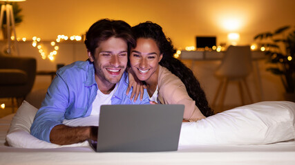 Spouses Watching Film On Laptop Lying In Bed At Home