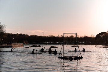 Silhouettes of people playing kayak polo during sunset